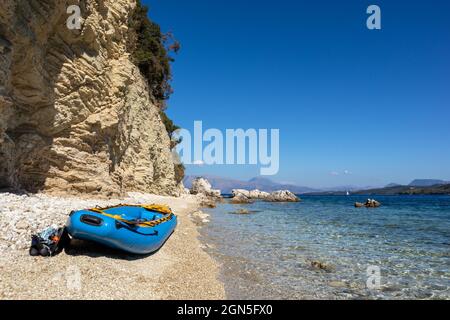 Yellow raft boat on white pebble beach with blue clear calm Ionian Sea bay. Scenic rocky cliffs coast. Lefkada island in Greece. Idyllic travel activi Stock Photo