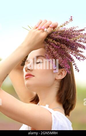 Beautiful young woman with bouquet of summer flowers outdoors Stock Photo