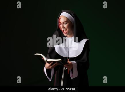 Crazy woman dressed for Halloween as nun with Bible on dark background Stock Photo