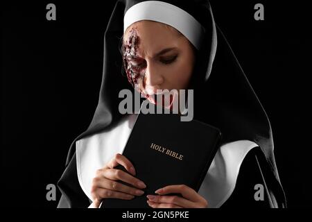 Woman dressed for Halloween as nun with Bible on dark background Stock Photo