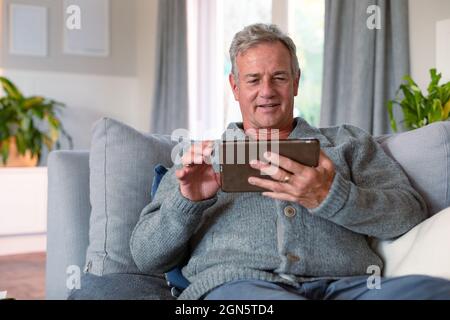 Happy caucasian senior man sitting on sofa and using tablet Stock Photo