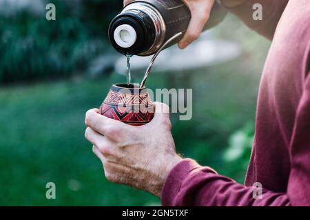 Man preparing a mate with hot water. Gourd mate with yerba inside. Middle age latin american man enjoying at the sunset outdoors. Stock Photo