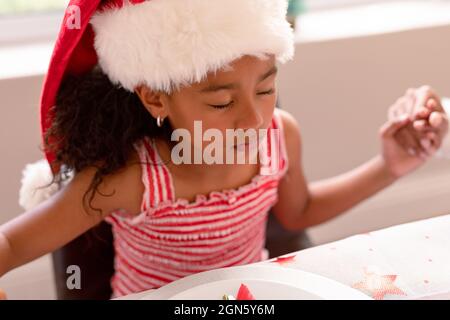 African american girl wearing santa hat praying at christmas table Stock Photo