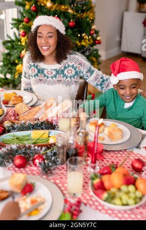 Happy african american mother and son wearing santa hats sitting at christmas table Stock Photo