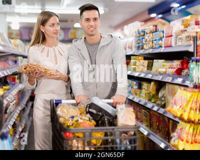 Young loving couple making purchases together, choosing cookies in grocery store Stock Photo