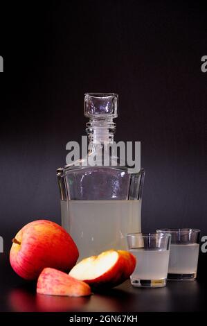 Apple Calvados, a strong alcohol in a glass bottle and two glasses with fruit pieces on a black background. Close-up. Stock Photo