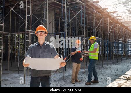Architect, Engineer, Contractor, or Construction manager holding blueprint standing with a group at a construction site. Stock Photo