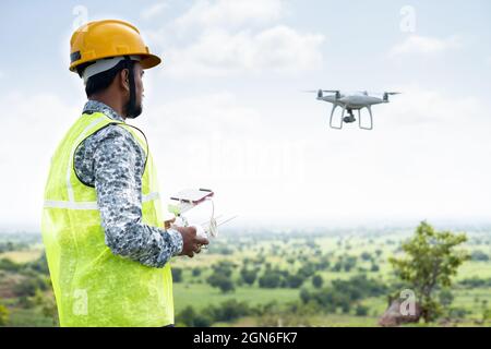 Focus on Pilot, Pilot with safety hardhat flying drone using remote controller - Concept of engineer doing aerial survey or inspection using UAV. Stock Photo