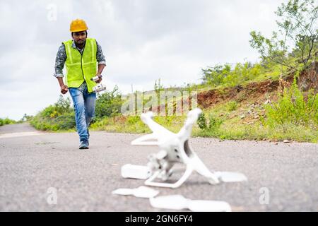 Focus on Pilot, Worried drone operator running in hurry near crashed drone on road - concept of UAV damage or accident while flying. Stock Photo