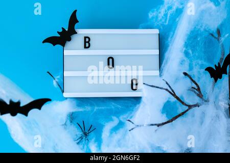 Lightbox with word BOO and halloween party decorations. Bats on dry tree branch with spider net for Halloween on blue background. Top view flatlay Stock Photo