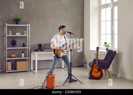 Rock musician singing into microphone and playing on electric guitar plugged in amplifier Stock Photo