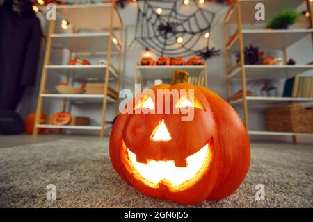 Close up of carved Jack-o-lantern standing on carpet in room with Halloween decor. Stock Photo