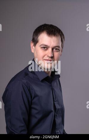 Portrait of a white European brunet man in a gray graphite shirt looking at the camera. Stock Photo