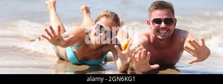 Joyful man and woman in sunglasses lie on wet sand near sea Stock Photo