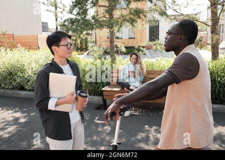 Horizontal side view medium portrait of young African American man and Asian woman meeting each other outdoors greeting each other and talking about something Stock Photo