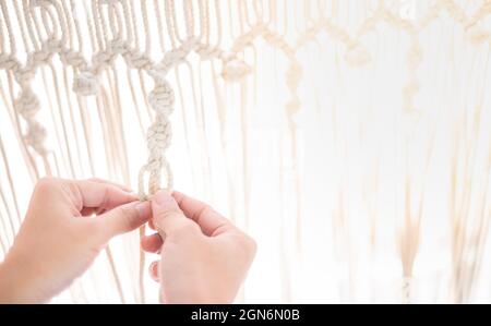 Female hand-making Macramé with the light beige rope and texture pattern for relaxing. And DIY natural decoration concept in the interior. Stock Photo
