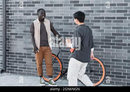 Horizontal long shot of handsome young African American man standing against brick wall and unrecognizable woman walking by greeting each other outdoors Stock Photo
