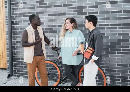 Modern African American guy and his female co-workers standing together outdoors talking about something during coffee break time Stock Photo