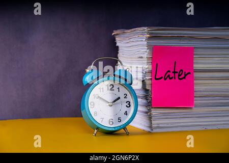 Business concept. Layout of alarm clock, stack of papers and note with text Later reference to procrastinate Stock Photo