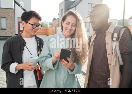 Horizontal medium portrait of three ethnically diverse friends hanging out together watching something in Internet on smartphone Stock Photo