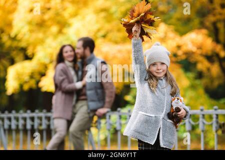 Family walk in autumn park. Loving parents of little girl hug outdoors in forest with colorful trees Stock Photo