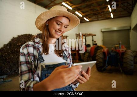 Caucasian female farmer smiling standing in shed holding digital tablet Stock Photo