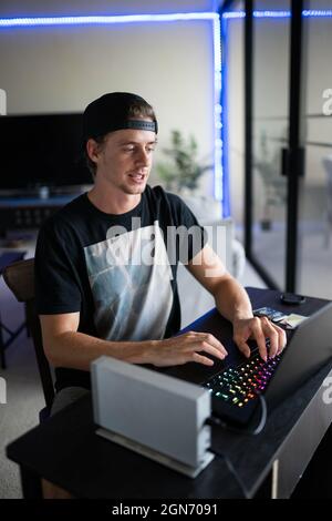 Young Caucasian man sitting at his desk and gaming on a laptop Stock Photo