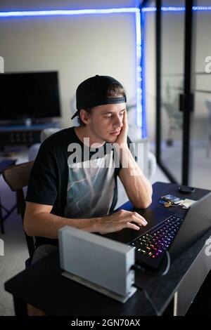 Bored young Caucasian man sitting at his desk and gaming on a laptop Stock Photo