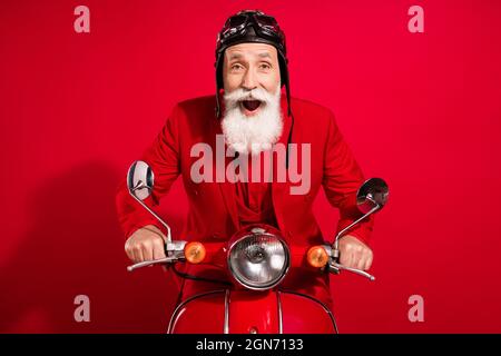 Photo of excited funky santa claus ride bike omg reaction open mouth wear goggles helmet suit on red color background Stock Photo