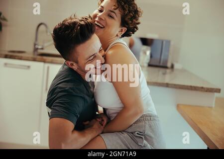 Romantic queer couple laughing cheerfully in the kitchen. Happy young queer couple having fun together indoors at home. Cheerful young LGBTQ+ couple b Stock Photo