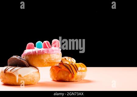 Photograph of three donuts decorated with jelly beans and drawn with chocolate.The photo is taken in horizontal format on a cream colored cardboard an Stock Photo