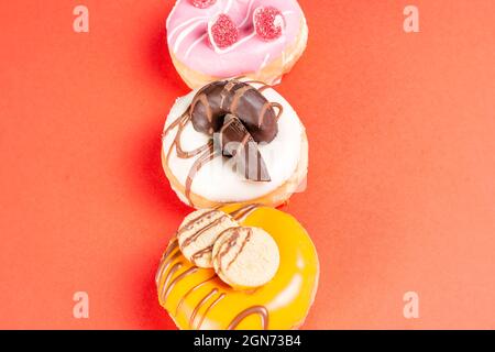 Photo of 3 donuts decorated with cookies and jelly beans on a red background.The donuts are dipped in strawberry chocolate, dark chocolate and white c Stock Photo