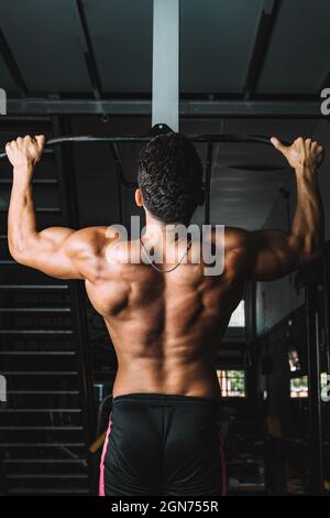 Vertical photo of the back of strong male doing pull-ups in a gym Stock Photo