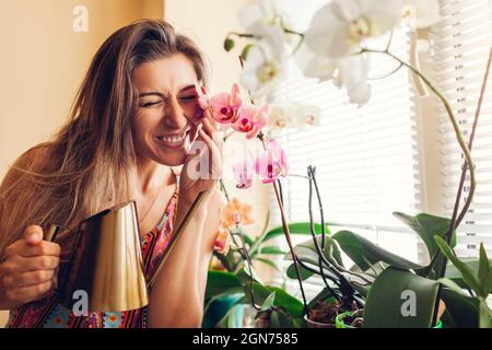 Happy woman touching orchids on window sill. Girl gardener taking care of home plants and flowers watering them. Stock Photo