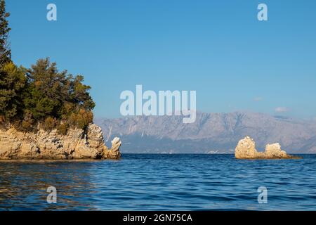 Sunset rocks in vivid blue water of Ionian Sea with rocky green cliffs and bright sky. Nature of Skorpios island near Lefkada in Greece. Summer vacati Stock Photo