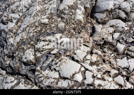 White and black big marble rock material with cracks close-up texture. Light stone surface pattern details in sunny Greece Stock Photo