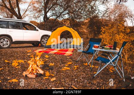 camping autumn place with bonfire and portable chairs no people. car on background Stock Photo