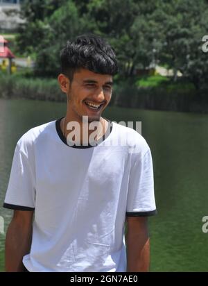 Portrait shot of a Indian young guy standing and smiling beside of lake with wearing white t-shirt Stock Photo