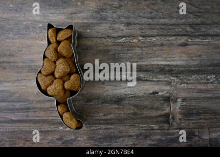 Cat shaped cookie cutter filled with heart shaped cat food on a wooden plate. Stock Photo