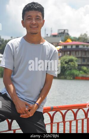 Portrait of a Ladakhi (North Indian) young guy sitting on safety barrier by lake and looking at camera Stock Photo