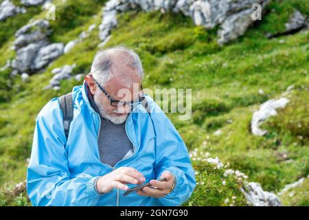 Elderly man along a mountain trail wearing eyeglasses and looking at his smartphone Stock Photo