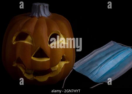 halloween in the age of coronavirus - pumpkin and face mask on black background Stock Photo