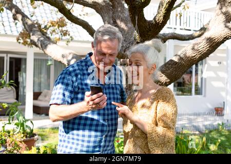 Happy caucasian senior couple using smartphone in front of house Stock Photo