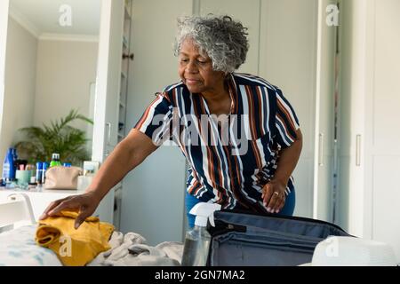 Focused african american senior woman packing suitcase in bedroom Stock Photo