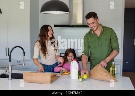 Happy caucasian parents and daughter unpacking groceries in kitchen Stock Photo