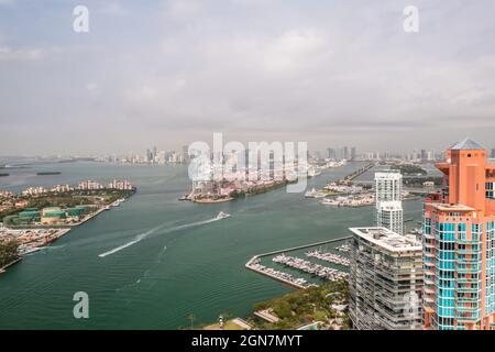 Incredible aerial view over the Miami shipping channels with the skyline on the horizon beyond and cloudy sky above as boats and ferries travel. Stock Photo