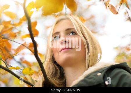 Beautiful young woman enjoying nature, smiling and looking up, framed by gold autumn leaves Stock Photo