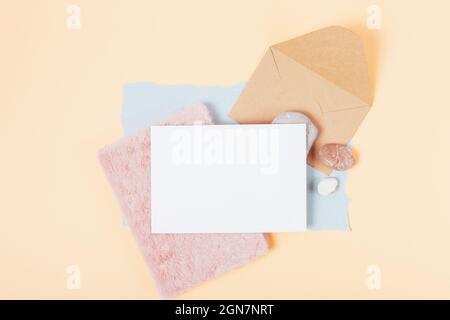 White blank paper card with fluffy notebook, natural stones and brown envelope on beige background, top view Stock Photo