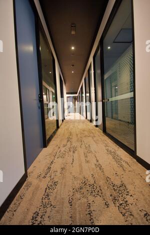SYDNEY, AUSTRALIA - Feb 14, 2020: A long corridor with speckled brown carpet, blue doors and glass walls, in a modern office in Sydney Stock Photo