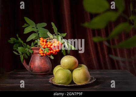 Rowan branch with berries and green apples on dark wooden background and textile with copy space Stock Photo